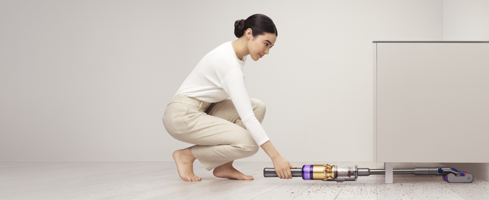 Woman using Dyson Omni-glide™ vacuum to clean under a cupboard.